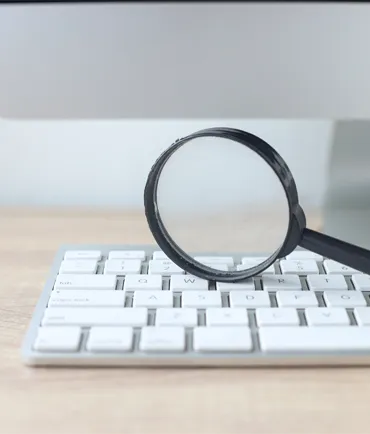 A magnifying glass on top of a computer keyboard representing SEO